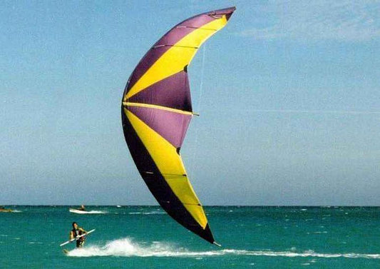 Vintage photo of a kitesurfer riding a board with one of the original kites and bars.