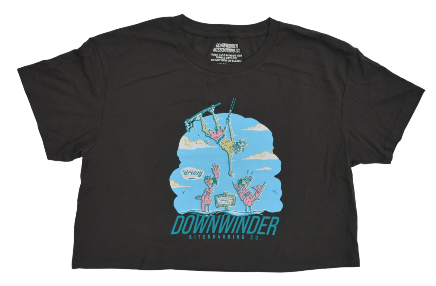 Women's dark grey "respekt the localz" kiteboarding crop top. Graphic shows a cartoon man doing a flip and high-fiving a cartoon flamingo. The shirt says Downwinder Kiteboarding Col